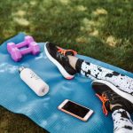 Focused workout setup outdoors with mat, dumbbells, phone, and water bottle.